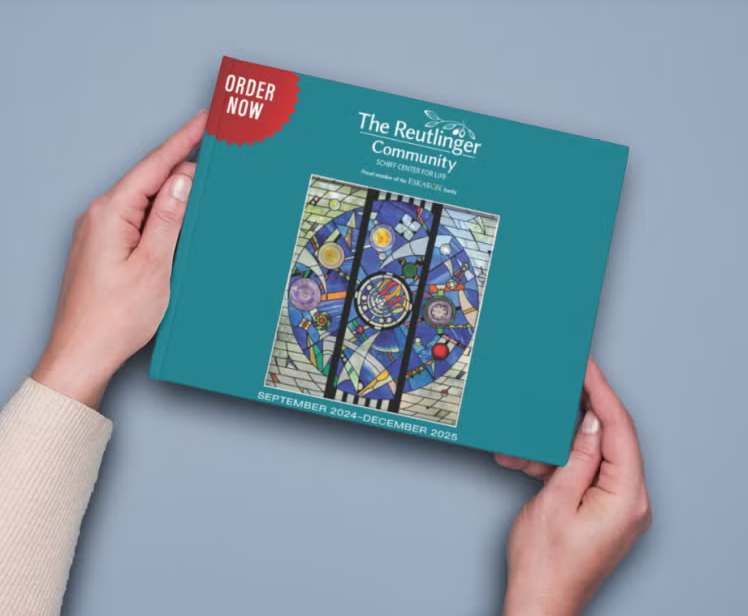 A person holds a teal book titled The Reutlinger Community with a colorful mosaic artwork on the cover and a red “Order Now” label. The bottom text reads “September 2024–December 2025.”.